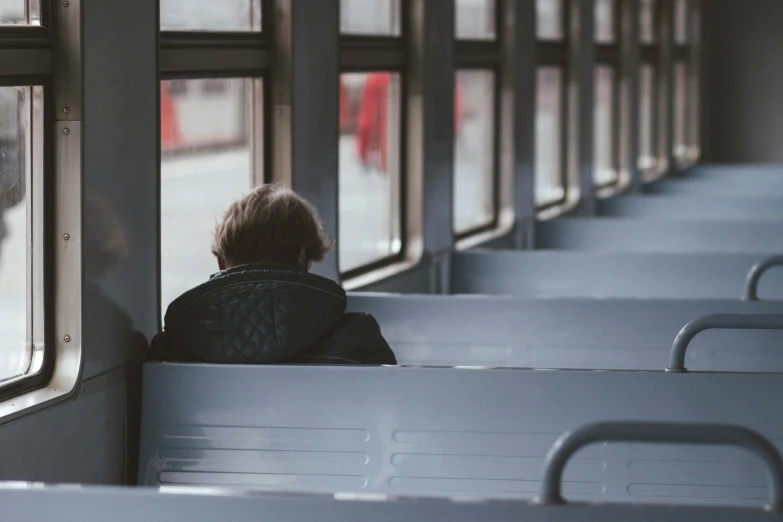 a person sitting in a train looking out the window, buses, lone person in the distance, teen boy, facing away from camera