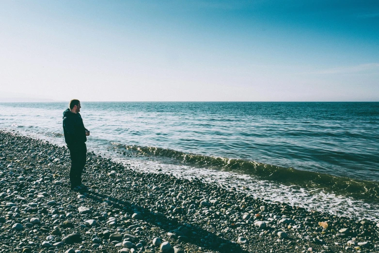 a person standing on a beach next to the ocean, black sea, pondering, landscape photo, profile picture 1024px