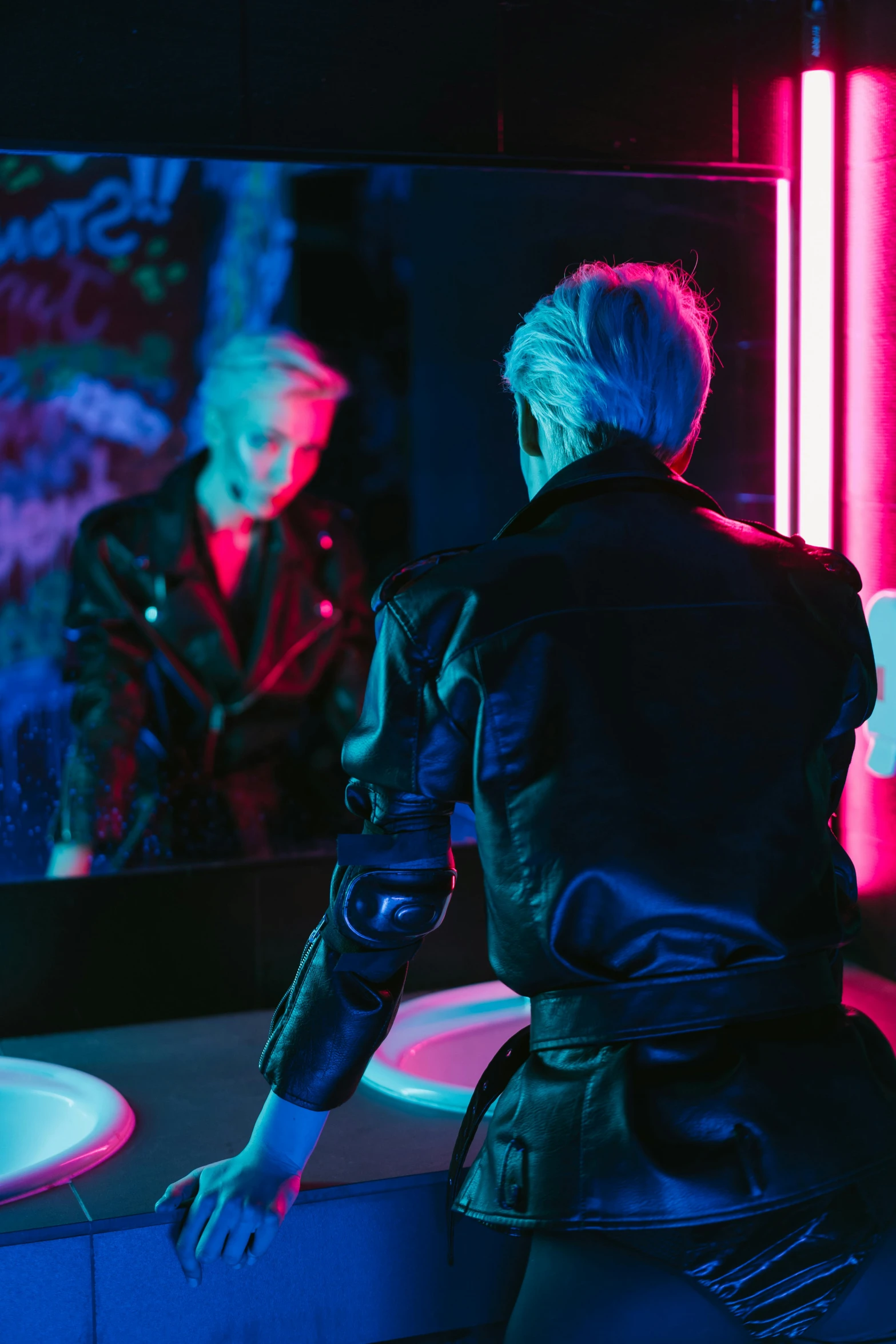 a woman standing in front of a mirror in a bathroom, cyberpunk art, trending on pexels, short platinum hair tomboy, a man wearing a black jacket, soft calm warm neon atmosphere, vergil