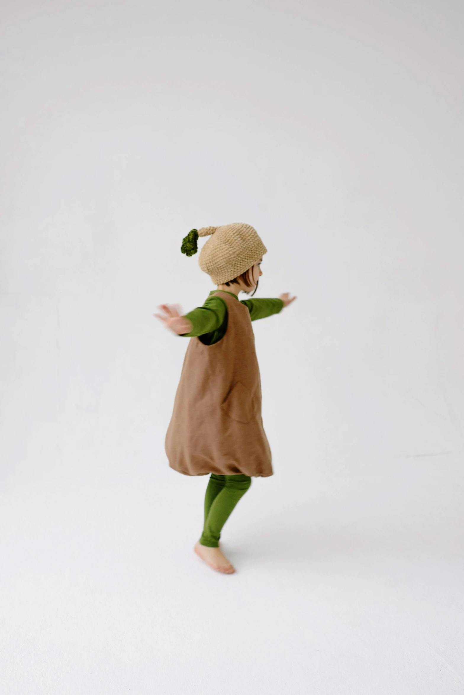 a little girl that is standing in the snow, an album cover, inspired by Kate Greenaway, unsplash, renaissance, green and brown clothes, avacado halloween costumes, with his back turned, baggy clothing and hat