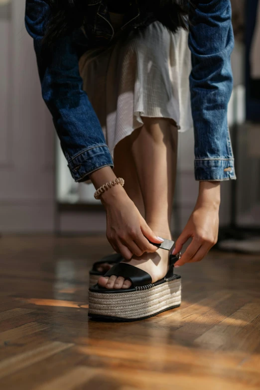 a woman is tying up her shoes on the floor, birkenstock sandals, vanta black, platforms, collection product