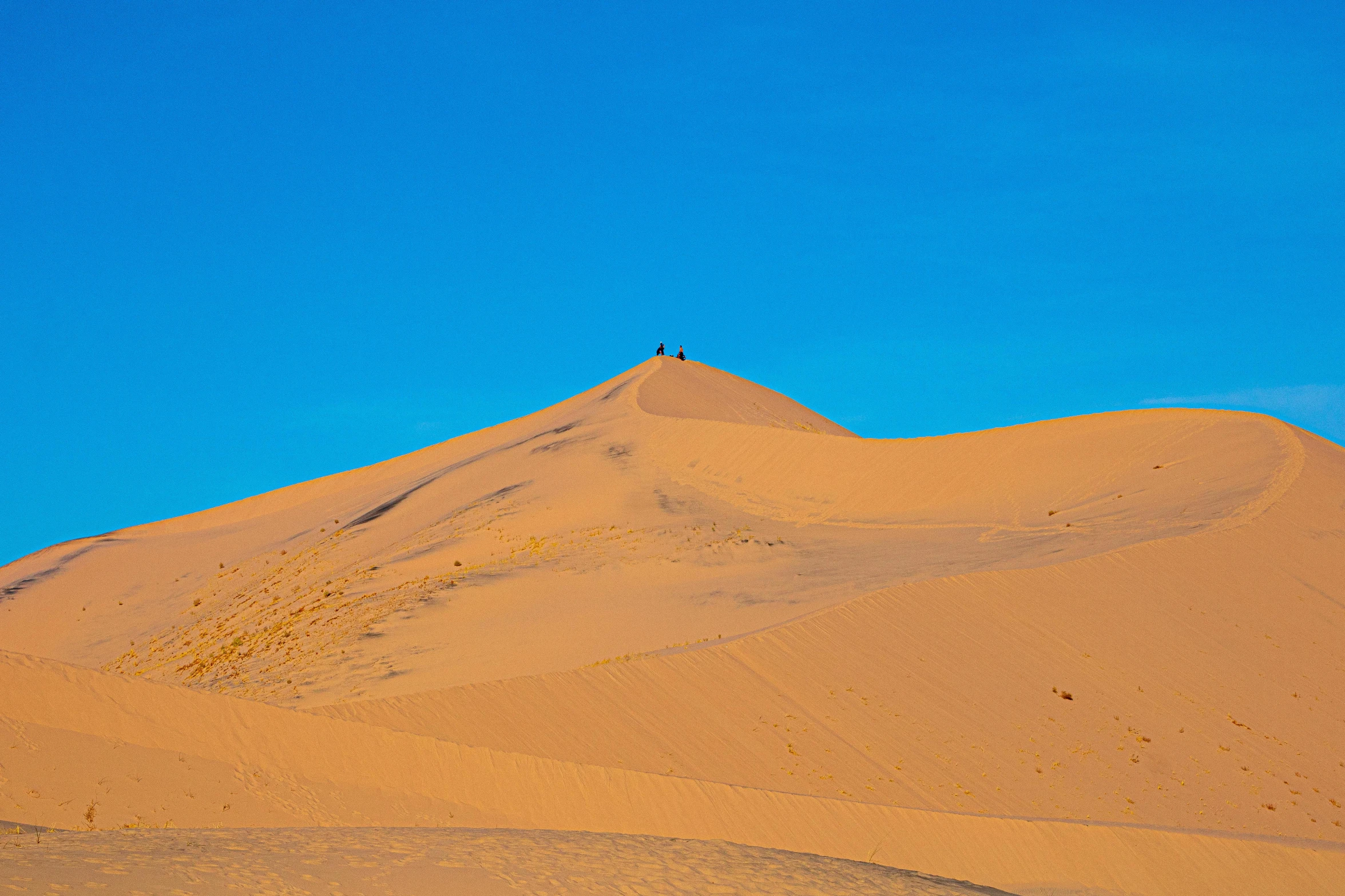 a person riding a horse in the desert, some orange and blue, sand dune, background image, distant photo