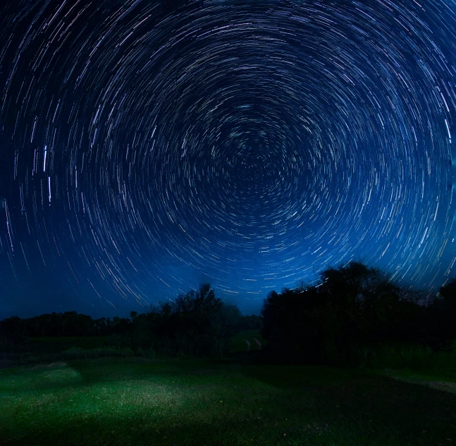 star trails in the night sky over a green field, pexels contest winner, land art, glowing tiny blue lines, circular, many stars, half turned around