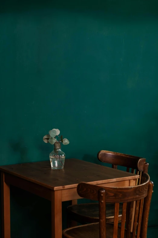 a wooden table with a vase of flowers on top of it, a minimalist painting, by Elsa Bleda, trending on unsplash, emerald color palette, studio medium format photograph, classroom background, 1 9 2 0 s furniture