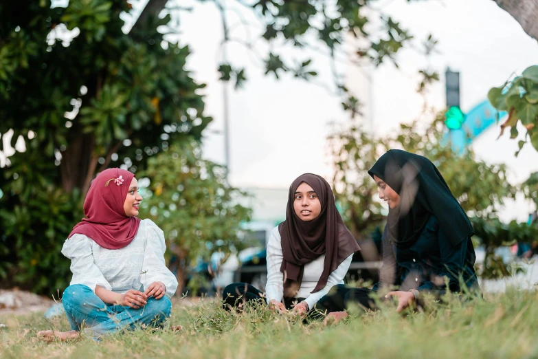 a group of women sitting on top of a lush green field, by Ella Guru, unsplash, hurufiyya, in a city square, malaysian, profile image, the three moiras