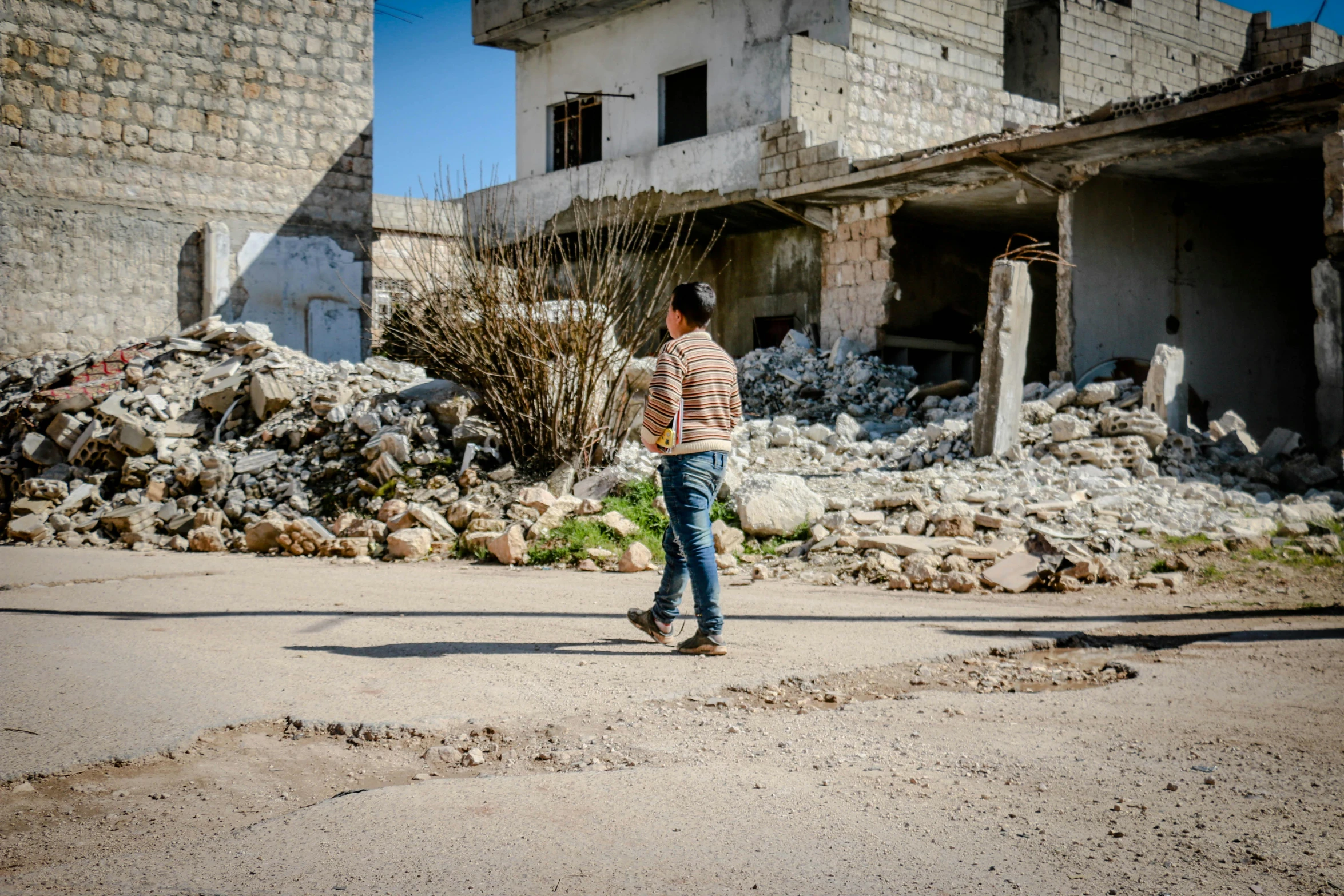 a man riding a skateboard down a street next to a building, happening, abandoned war torn village, profile image, rojava, standing on rocky ground