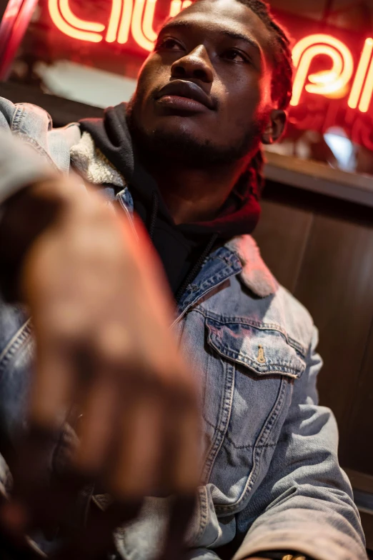 a man sitting in front of a neon sign, by Amos Ferguson, trending on pexels, denim jacket, sitting at the bar, ( ( theatrical ) ), playboi carti