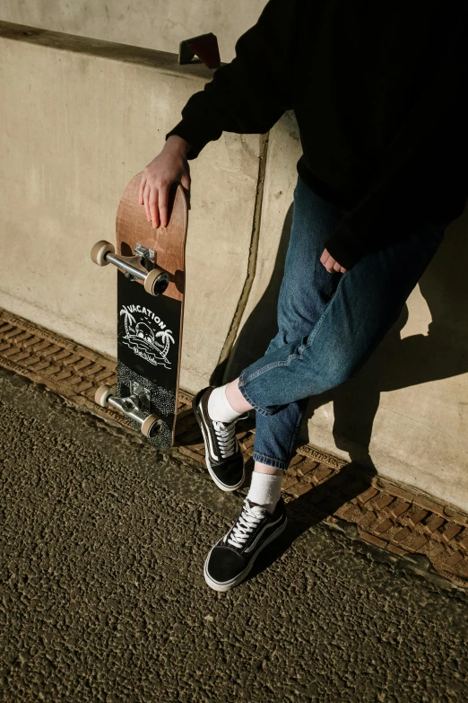 a person leaning against a wall with a skateboard, wearing jeans and a black hoodie, on a tree, leg high, federation clothing