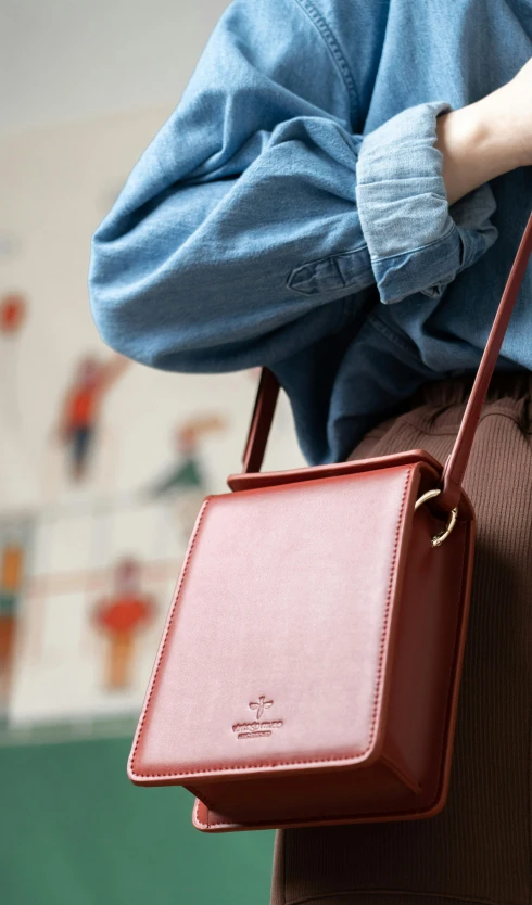 a woman in a blue shirt and brown pants holding a red purse, an album cover, trending on pexels, square, phone photo, detail shot, england