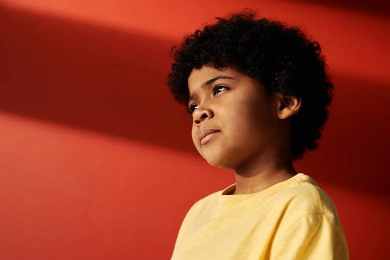 a young boy standing in front of a red wall, light brown skin, gradient yellow to red, looking off into the distance, compassionate