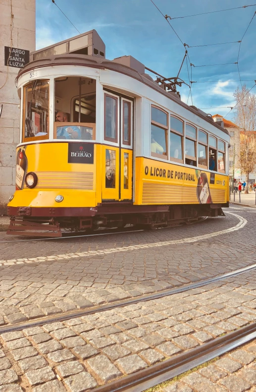 a yellow trolley traveling down a street next to a tall building, cobblestone roads, bay, profile image, tram