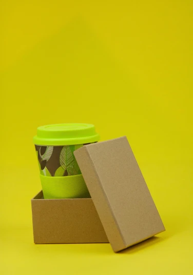a cup of coffee in a box on a yellow background, by Andries Stock, pexels, lime green, made of cardboard, protective, - 6
