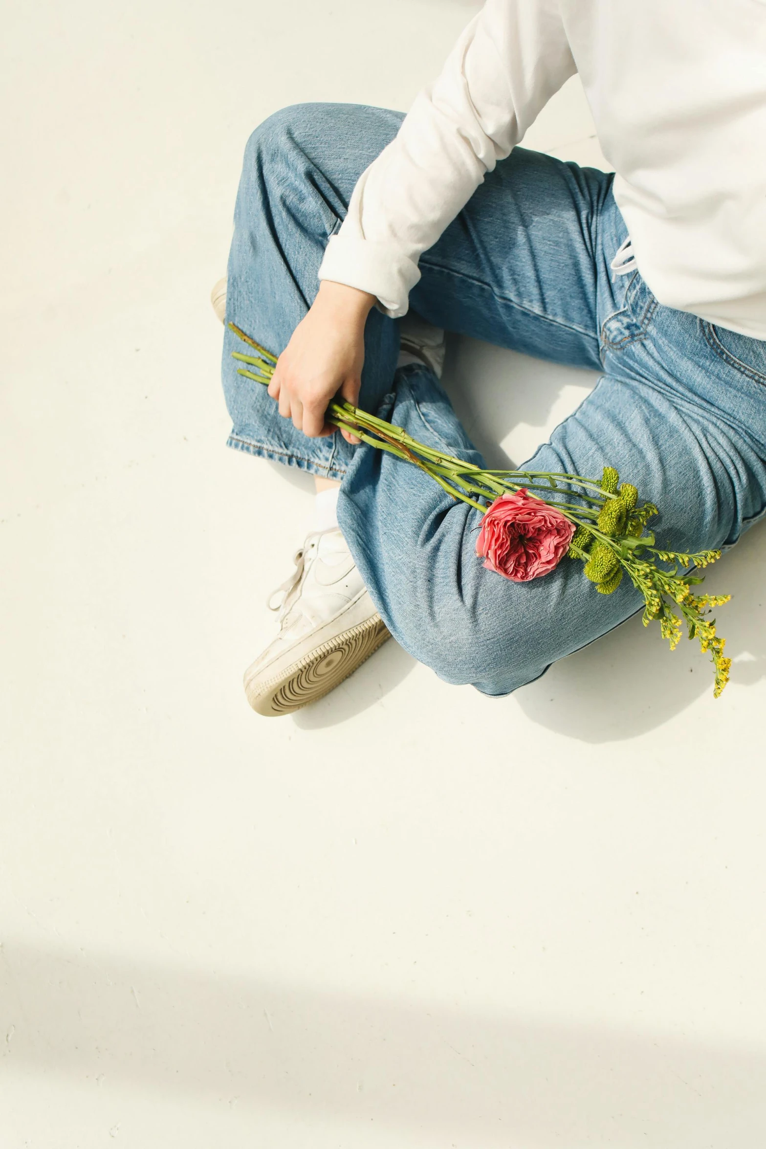 a person sitting on the ground with a flower in their hand, wearing jeans, white shirt and blue jeans