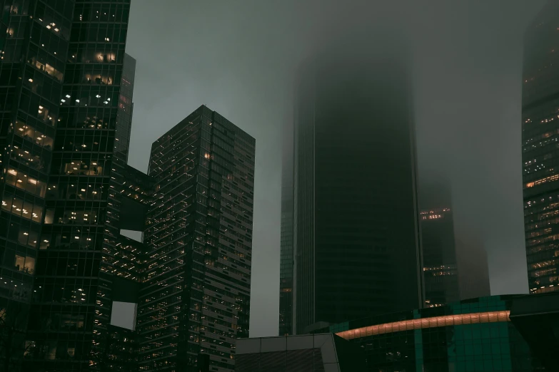 a group of tall buildings in a city at night, inspired by Elsa Bleda, pexels contest winner, hypermodernism, under a gray foggy sky, mossy buildings, foggy sky, instagram post