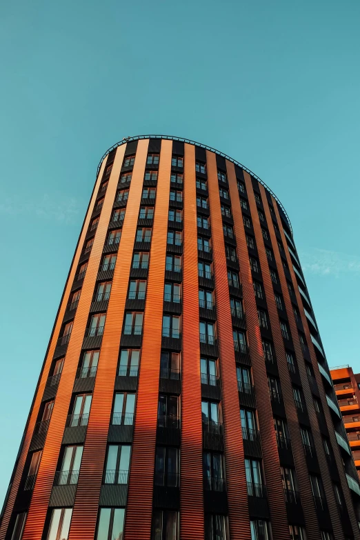 a tall building with many windows in front of a blue sky, by Sven Erixson, unsplash, red and brown color scheme, rounded roof, orange and black tones, apartment complex made of tubes