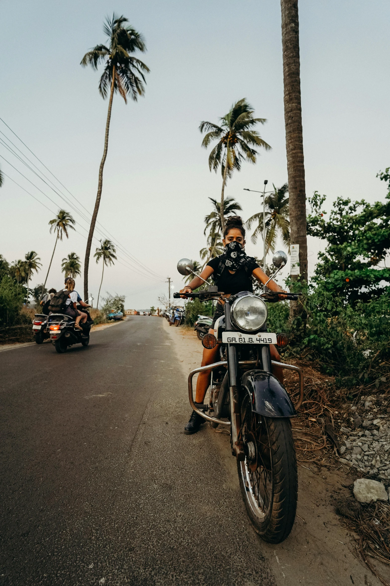 a man riding on the back of a motorcycle down a road, coconut trees, harley queen, profile image