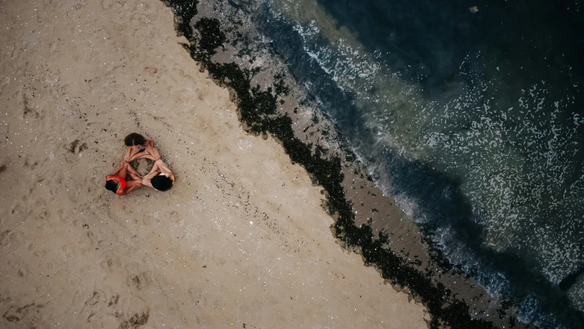 a couple of people laying on top of a sandy beach, by Adam Marczyński, pexels contest winner, aerial footage, ilustration, cinematic image