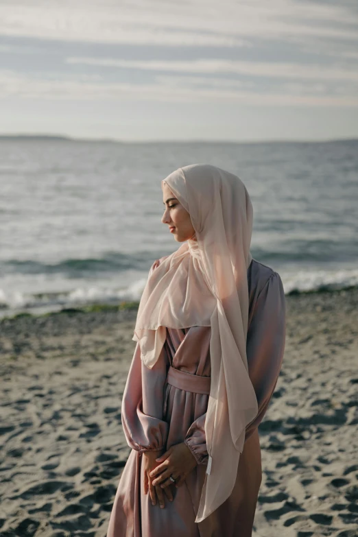 a woman standing on top of a sandy beach, inspired by Maryam Hashemi, unsplash contest winner, hurufiyya, pale pink and gold kimono, hijab, serious expression, near a jetty