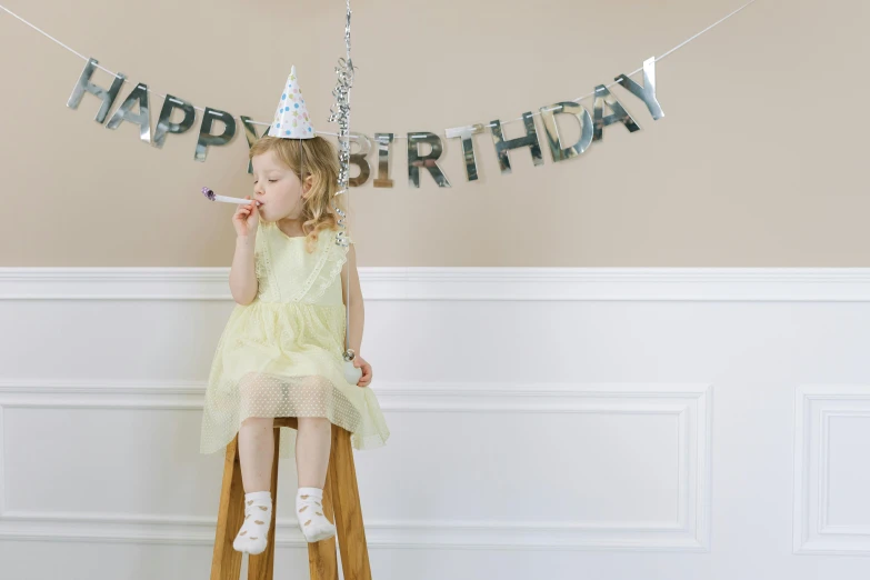 a little girl sitting on a stool in front of a happy birthday banner, pexels, fancy silver dress, background image, pals have a birthday party, profile image