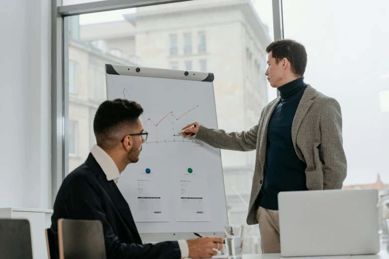 two men sitting at a table in front of a white board, pexels contest winner, giving a speech, people at work, charts, 1 4 9 3