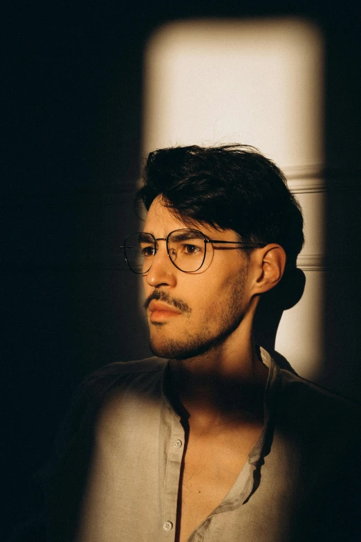 a man with glasses standing in front of a window, a character portrait, inspired by Camilo Egas, pexels contest winner, non binary model, low lighting, mark edward fischbach, profile image