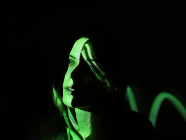 a woman that is standing in the dark, ambient green light, reflective faces, person in foreground, promo image