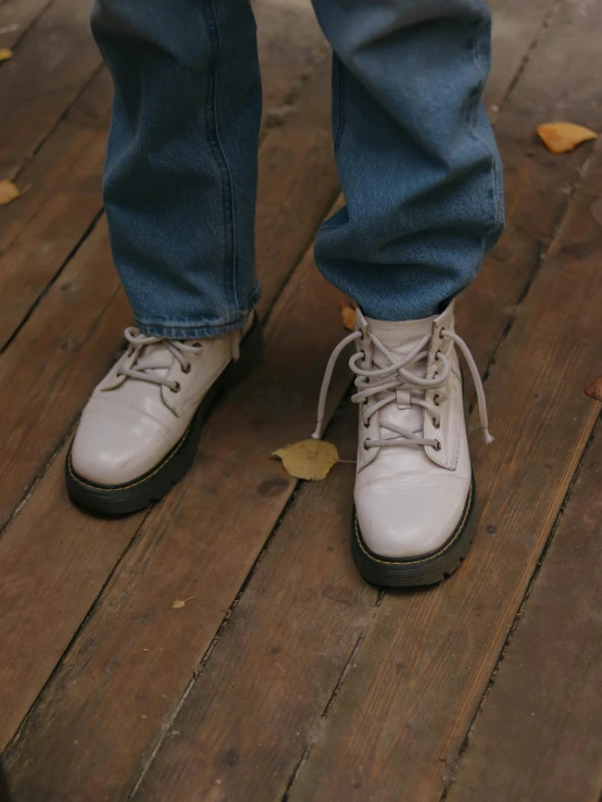a pair of white shoes sitting on top of a wooden floor, an album cover, inspired by Sarah Lucas, trending on unsplash, wearing tall combat boots, pale grey skin, closeup - view, autumn