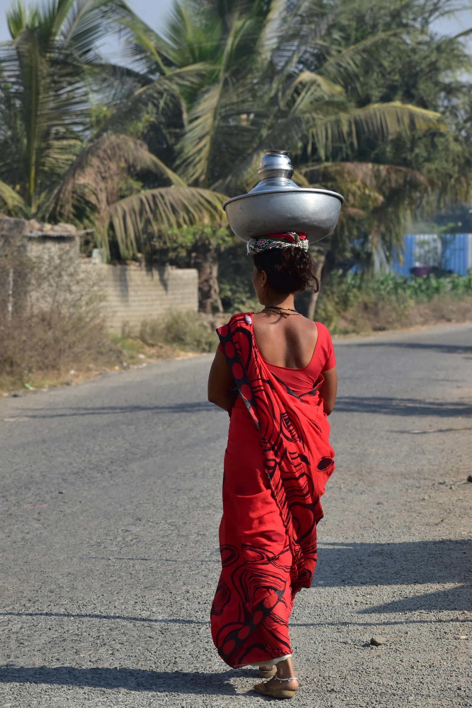 a woman walking down a street carrying a pot on her head, by Hannah Tompkins, samikshavad, water to waste, girl wears a red dress, in the countryside, update