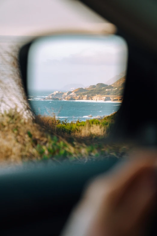 a view of the ocean through a rear view mirror, a picture, by Niko Henrichon, trending on unsplash, hollister ranch, slide show, person in foreground, field of view