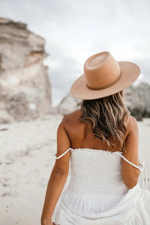 a woman in a white dress and hat walking on the beach, trending on pexels, caramel. rugged, back of head, canyon, skincare