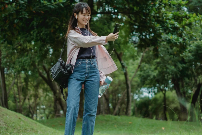 a woman standing on top of a lush green field, a picture, trending on pexels, happening, kawaii shirt and jeans, holding a very advance phone, student, people outside walk