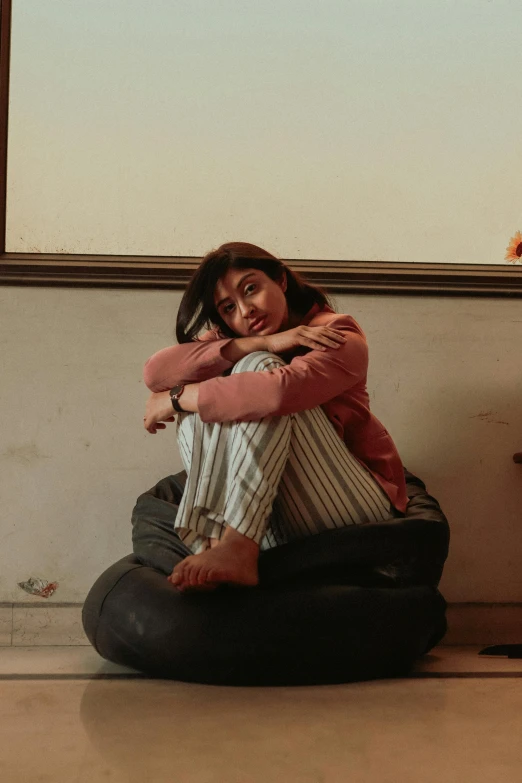 a woman sitting on a bean bag in front of a window, inspired by Elsa Bleda, pexels contest winner, maisie williams, hugging her knees, zaha hadi, ( ( theatrical ) )