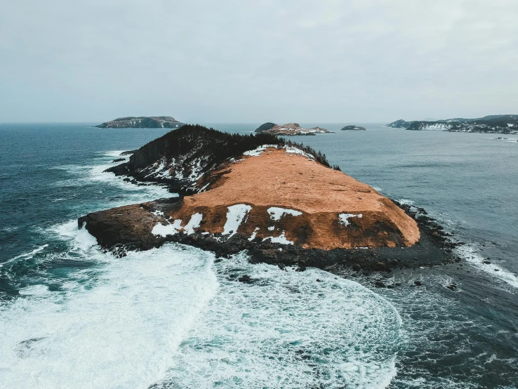 a small island in the middle of the ocean, by Kyle Lambert, pexels contest winner, land art, brown, large cape, quebec, curvacious