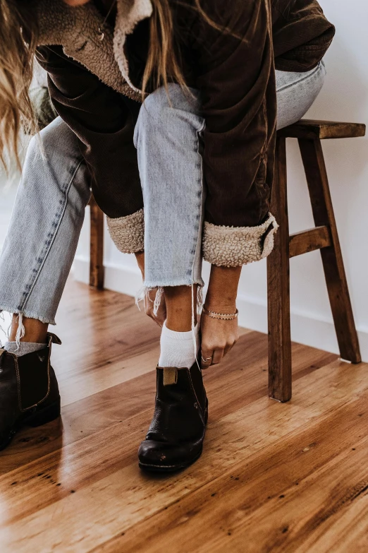 a woman sitting on top of a wooden chair, by Nina Hamnett, trending on pexels, jeans and boots, foot wraps, browns and whites, furry style