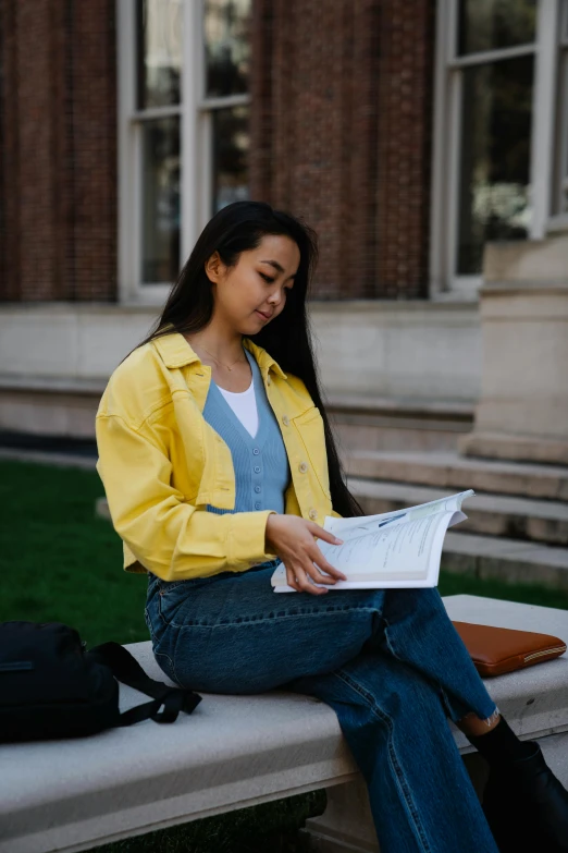 a woman sitting on a bench reading a book, trending on unsplash, academic art, yellow clothes, wearing a jeans jackets, asian descent, wearing an academic gown