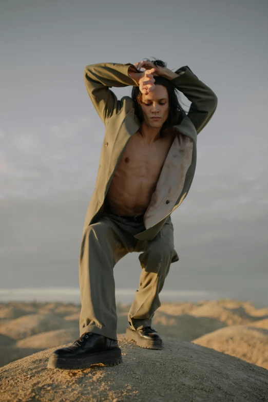 a man standing on top of a large rock, an album cover, trending on pexels, renaissance, portrait of combat dancer, non binary model, wearing a track suit, covered in sand