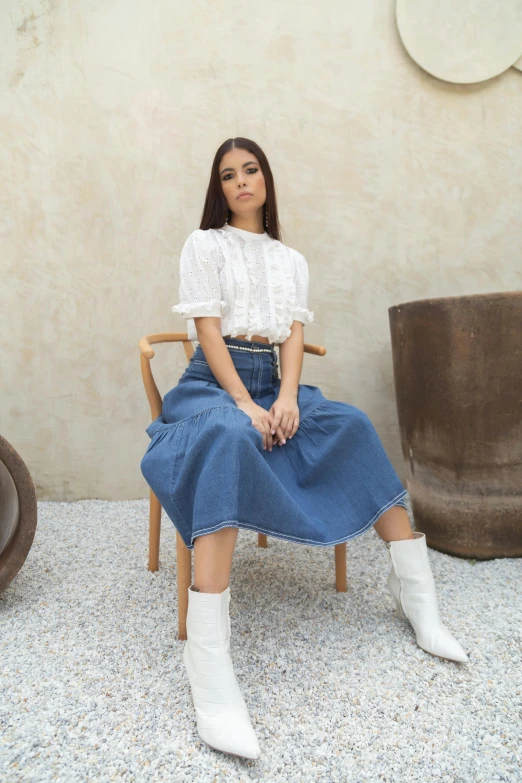 a woman sitting on top of a wooden chair, white shirt and blue jeans, wearing white skirt, wearing boots, cindy avelino