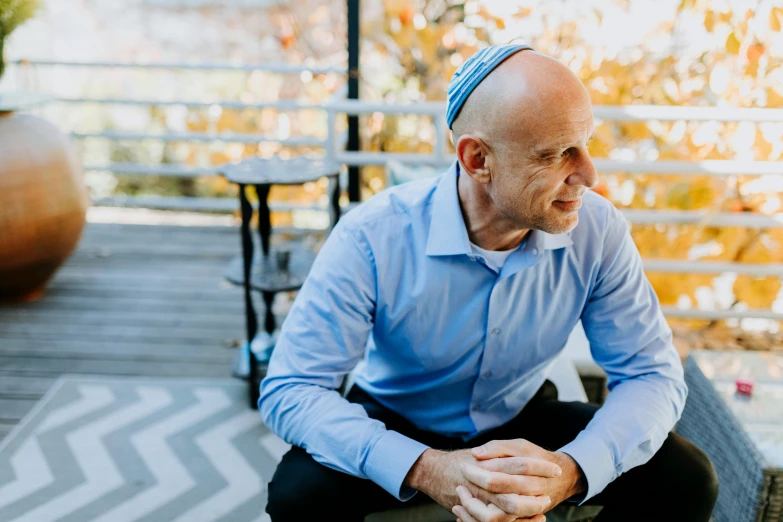 a man in a blue shirt sitting on a bench, hebrew, bald on top, compassionate, profile image