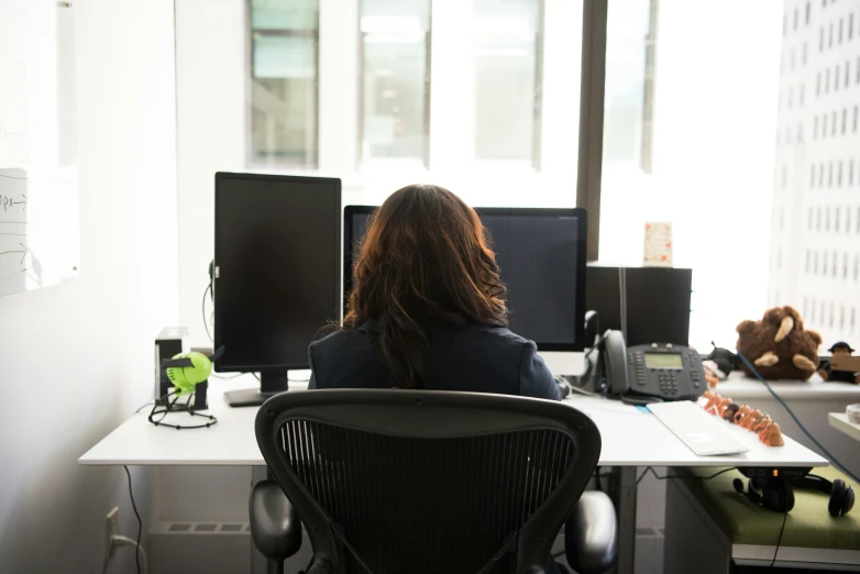 a woman sitting at a desk in front of a computer, by Jacqui Morgan, unsplash, back - view, lachlan bailey, coworkers, high - angle view