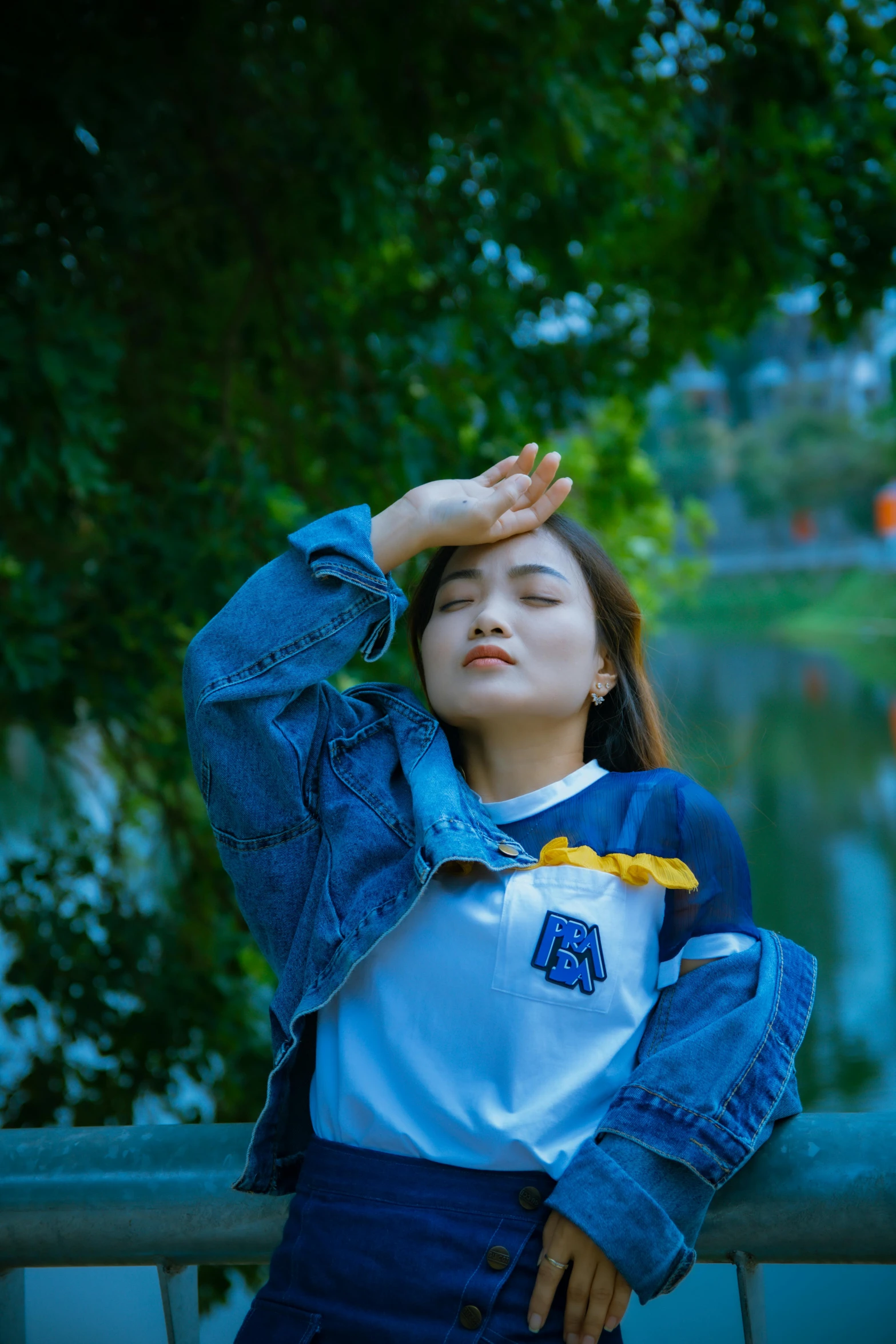 a woman standing on a bridge next to a body of water, an album cover, inspired by Yu Zhiding, unsplash, realism, wearing a blue jacket, asian features, doing a sassy pose, wearing sweatshirt