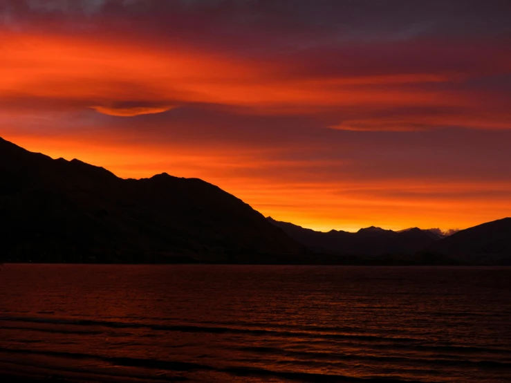 a sunset over a body of water with mountains in the background, by Charlotte Harding, pexels contest winner, hurufiyya, red cloud light, new zealand, orange and red lighting, boka