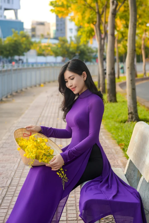 a woman sitting on a bench holding a basket of flowers, a picture, inspired by Ruth Jên, pexels contest winner, ao dai, purple and yellow, long sleeves, with a sleek spoiler