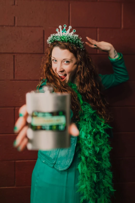 a woman in a green dress holding a drink, by Meredith Dillman, pexels contest winner, wearing a crown and green cape, holding a tin can, felicia day, curly haired