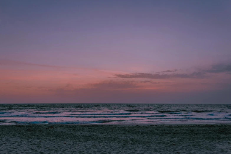 a man standing on top of a sandy beach next to the ocean, unsplash contest winner, minimalism, barely lit warm violet red light, evening at dusk, omaha beach, purple and pink