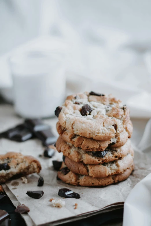 a stack of chocolate chip cookies next to a glass of milk, trending on pexels, modernism, powdered sugar, handcrafted, black, large cracks