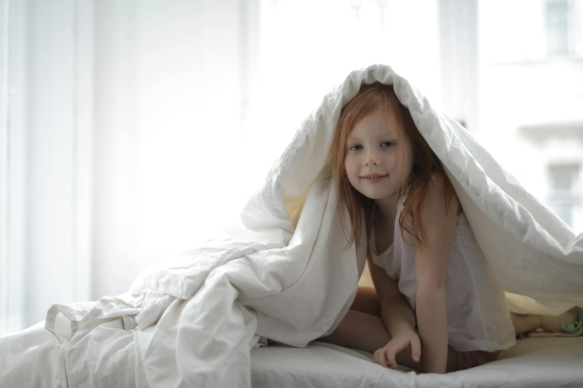 a little girl sitting on top of a bed under a blanket