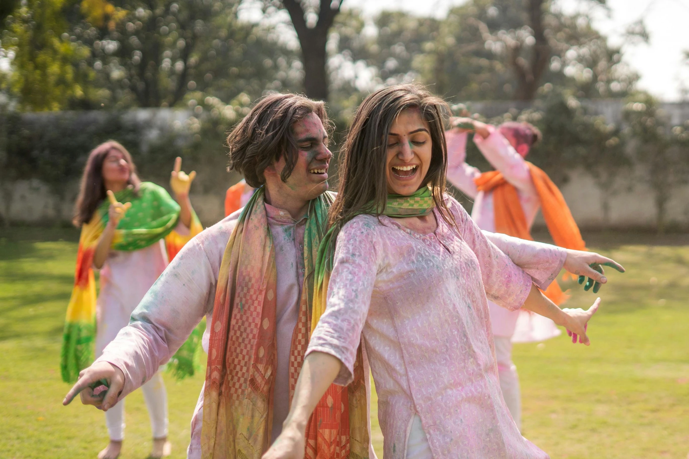 a couple of women standing on top of a lush green field, pexels contest winner, color field, dressed in a jodhpuri suit, wearing a tie-dye shirt, people dancing in background, wearing a fancy dress