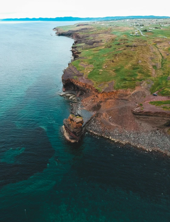 a large body of water next to a lush green hillside, by Thomas Furlong, pexels contest winner, happening, flying rocky island, red sand beach, high quality photo, looking down a cliff