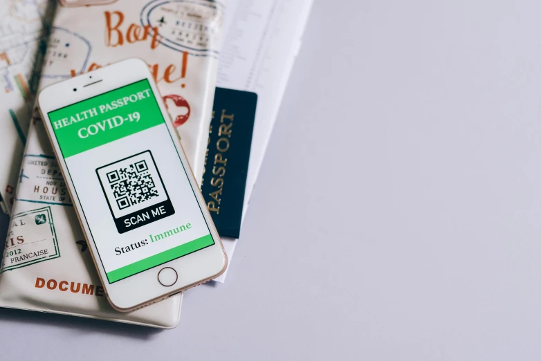 a cell phone sitting on top of a pile of papers, smartphone displays qr code, passport, green colored theme, covid