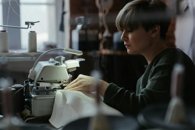 a woman working on a sewing machine in a factory, a portrait, inspired by Elsa Bleda, trending on unsplash, ignant, mary jane ansell, sustainable materials, wearing an apron